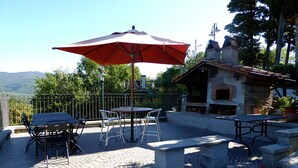An outdoor patio with a table and chairs, a red umbrella, and a stone oven. - Holiday Home in Montecarelli with Pool (Montecarelli)