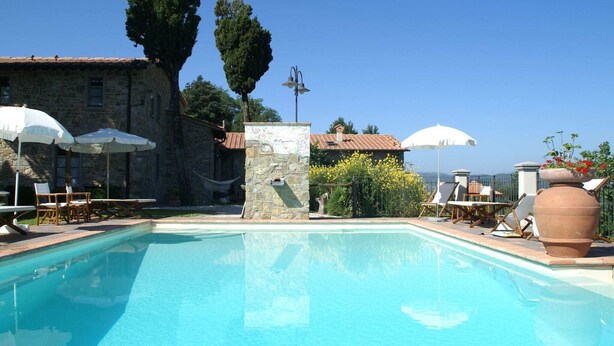 A swimming pool with lounge chairs and umbrellas, surrounded by stone buildings and trees. - Holiday Home in Montecarelli with Pool (Montecarelli)