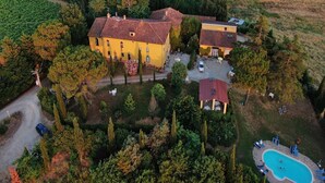 An aerial view of a countryside property with a large yellow building, a smaller attached structure, and a swimming pool surrounded by lounge chairs. - Farmhouse in Vinci near Leonardo's Birthplace (Vinci)