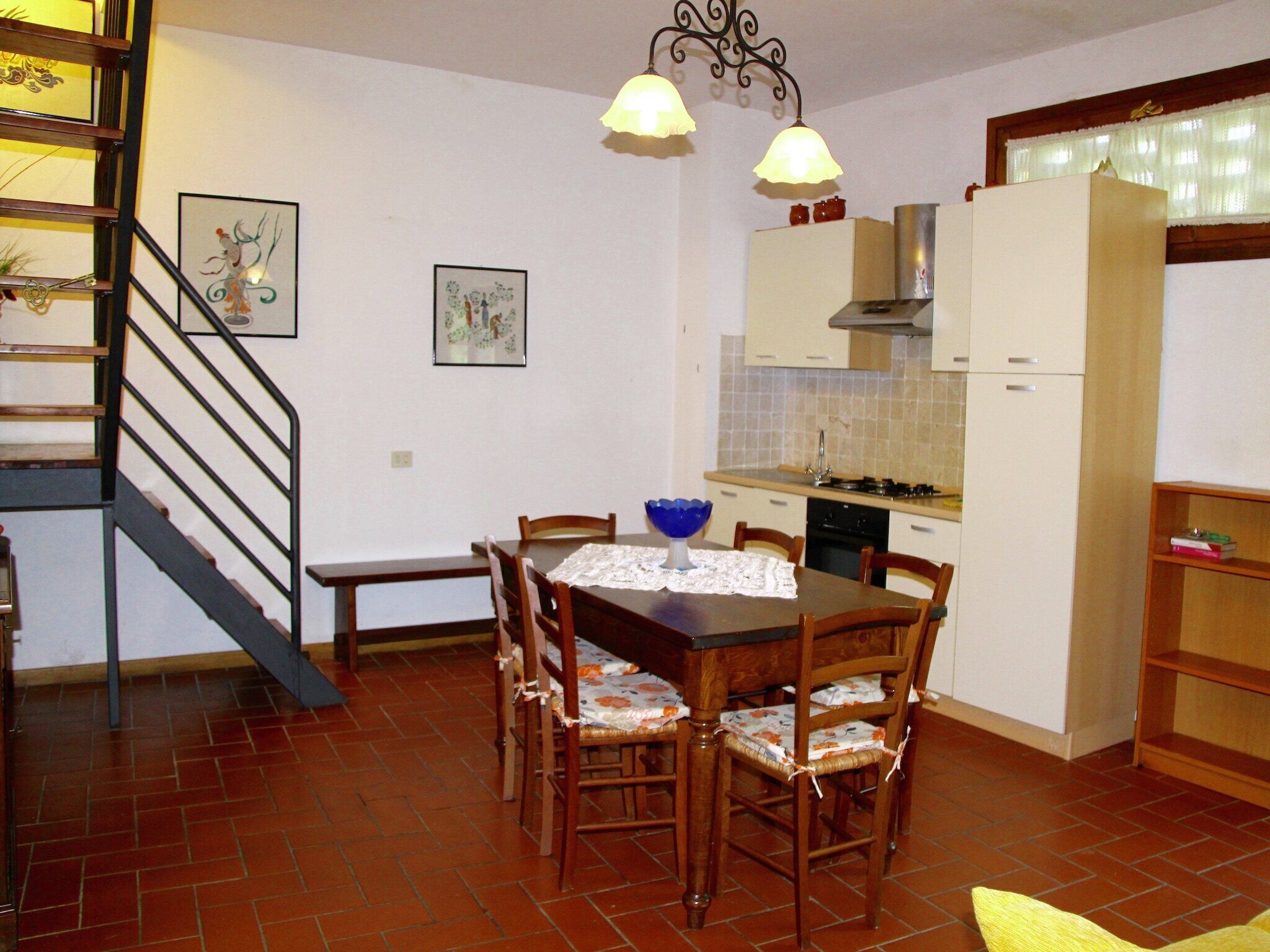 A compact kitchen with a dining table and chairs, a staircase, and a small bookshelf.