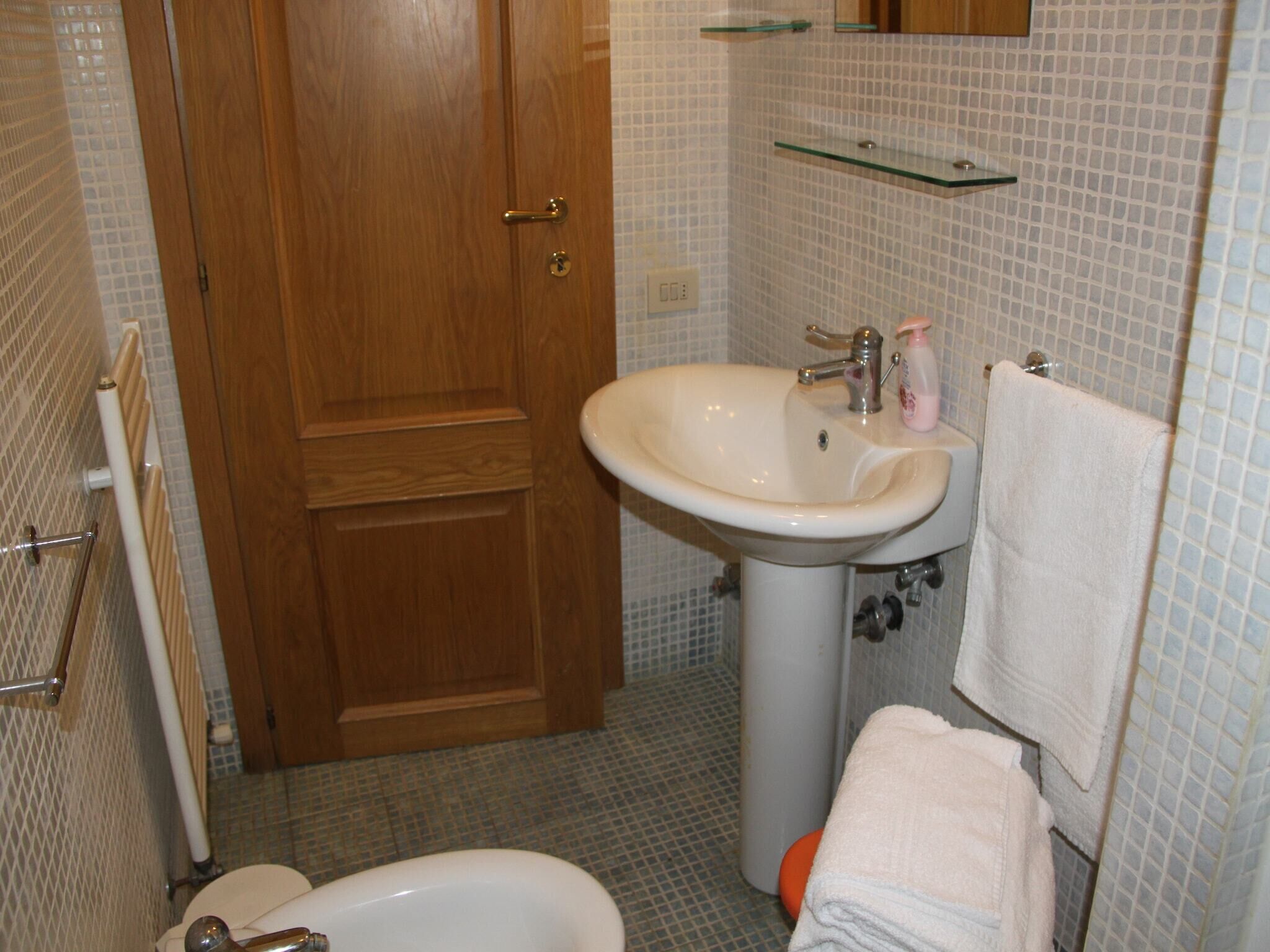 Un baño con puerta de madera, un lavamanos blanco con un espejo encima y un inodoro.