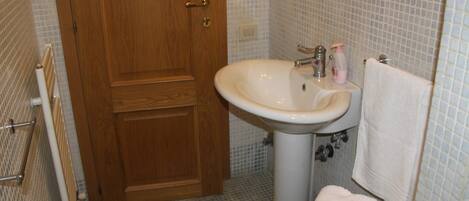 Un baño con puerta de madera, un lavamanos blanco con un espejo encima y un inodoro.