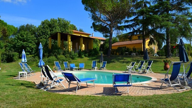 A pool area with lounge chairs and umbrellas, surrounded by greenery and a building with a tiled roof. - Farmhouse in Vinci near Leonardo's Birthplace (Vinci)
