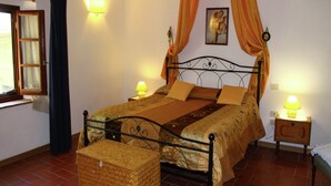 A bedroom with a four-poster bed, two bedside lamps, a wicker chest, and a window with curtains. - Farmhouse in Vinci near Leonardo's Birthplace (Vinci)