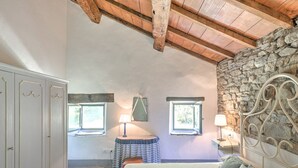 Un dormitorio con una cama grande, dos ventanas, una pared de piedra y un techo de madera.