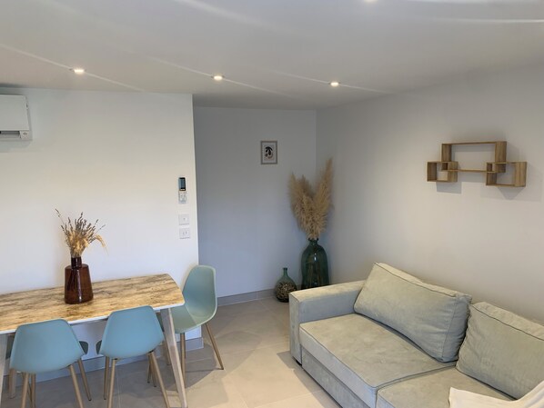 Una sala de estar moderna con un sofá de color claro, una mesa de centro de madera y dos sillas azul claro. Hay un jarrón decorativo con plumas de pampa sobre la mesa.