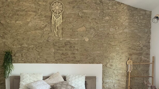 Ein Schlafzimmer mit einer Steinsandsteinwand, einem Bett mit gemusterten Betttextilien und einem dekorativen Traumfänger.