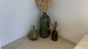 Ein Zimmerwinkel mit weißer Wand, einem gerahmten Bild und drei Vasen mit Trockenpflanzen.