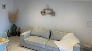 Ein Wohnzimmer mit grauem Sofa, einem kleinen runden Tisch und einer Vase mit Pampasgras.