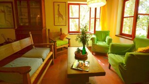 Una habitación acogedora con techo de madera, un sofá verde, una silla de madera, una pequeña mesa con una planta y una imagen de una jirafa en la pared.