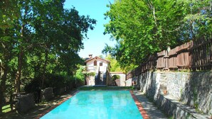 Una piscina con un muro de piedra en un lado y una valla de madera en el otro, que conduce a un edificio con tejado de tejas rojas.