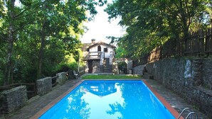 Ein rechteckiger Pool mit Steinbordierung, umgeben von einer Steinmauer und einem Holzzaun.