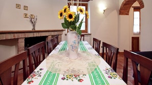 Ein Essbereich mit einem Tisch, gedeckt für vier Personen, einer Vase mit Sonnenblumen, Holzstühlen, einem Ziegelkamin und einem Ziegelbogen.