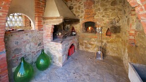 Ein rustikaler Backsteinofen mit Backsteinsschornstein, einem Steinkamin und einem Holzregal mit Flaschen.