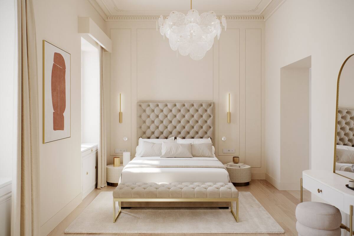Quarto com cabeceira estofada, uma cama grande, mesas de cabeceira, um banquinho, um espelho e um candelabro.