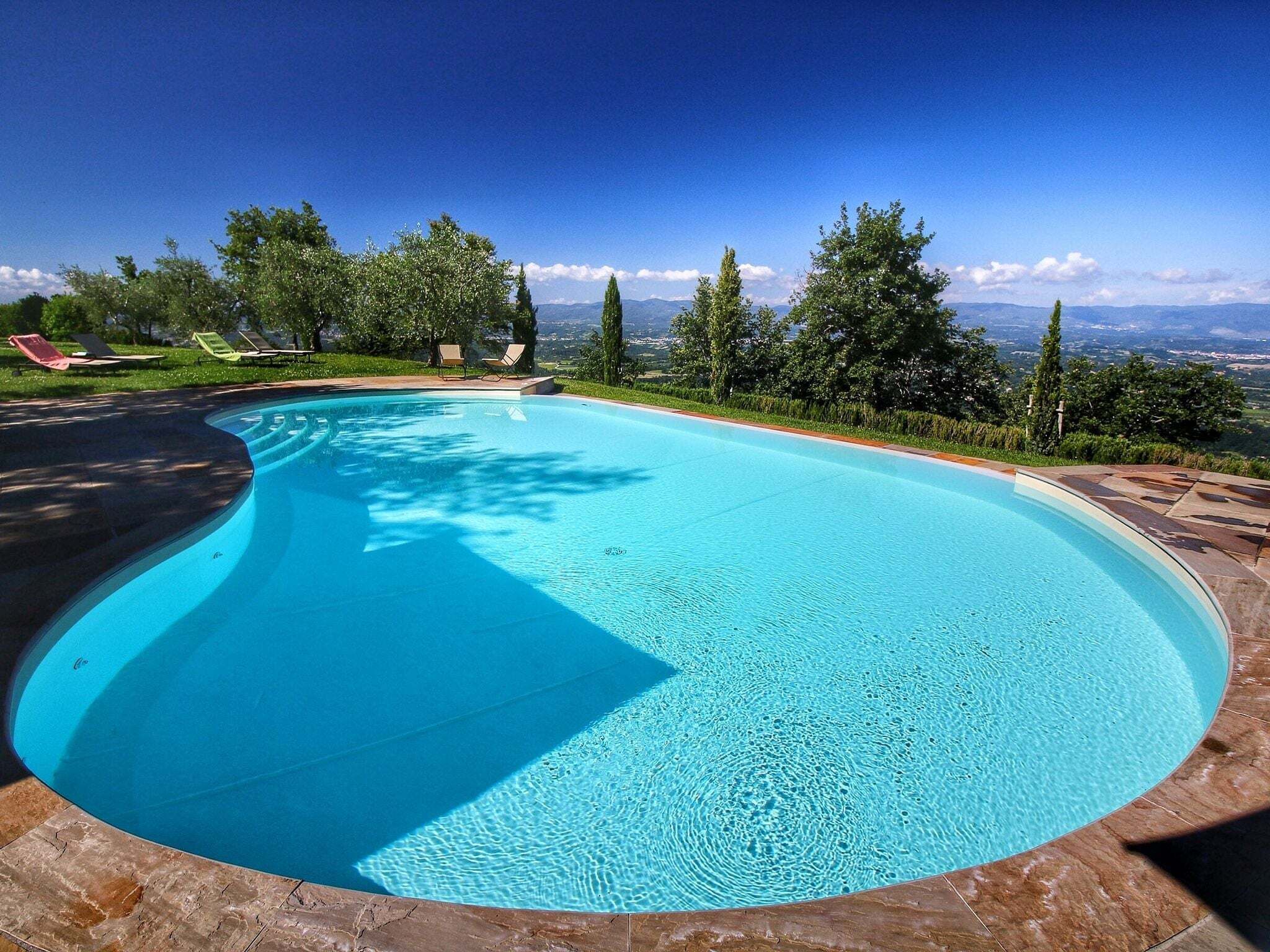 Une piscine aux bords incurvés, avec une eau d’un bleu cristallin, entourée d’une terrasse en pierre et de chaises longues.