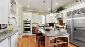 A modern kitchen with white cabinets, stainless steel appliances, a granite countertop, and a central island with stools. - The Houstonia, 3 bedroom single family home near DC (Arlington)