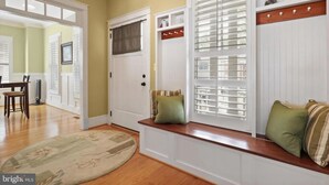 A room with a wooden bench, white shutters, and a door with a brown curtain. - The Houstonia, 3 bedroom single family home near DC (Arlington)