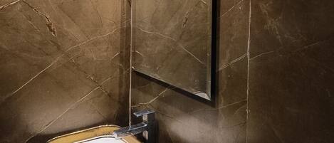 A bathroom with a marble wall, a sink with a mosaic design, and a mirror.