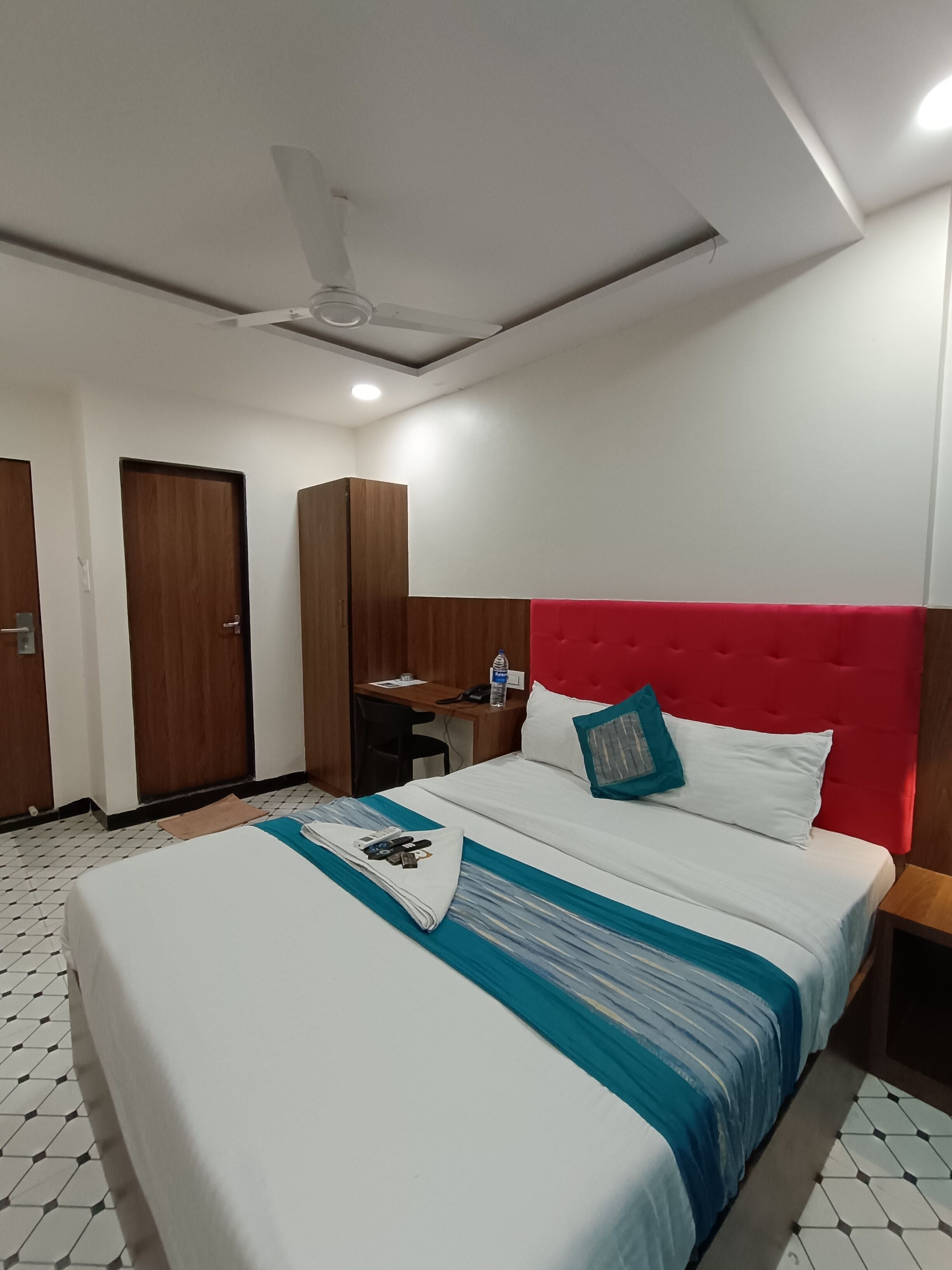 A hotel room with a bed, a desk, a chair, a wardrobe, and a ceiling fan.