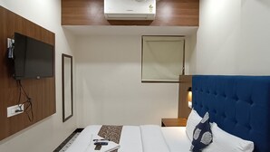 A hotel room with a bed, a TV mounted on the wall, an air conditioning unit, a bedside table, and a chair. - Hotel Best (Mumbai)