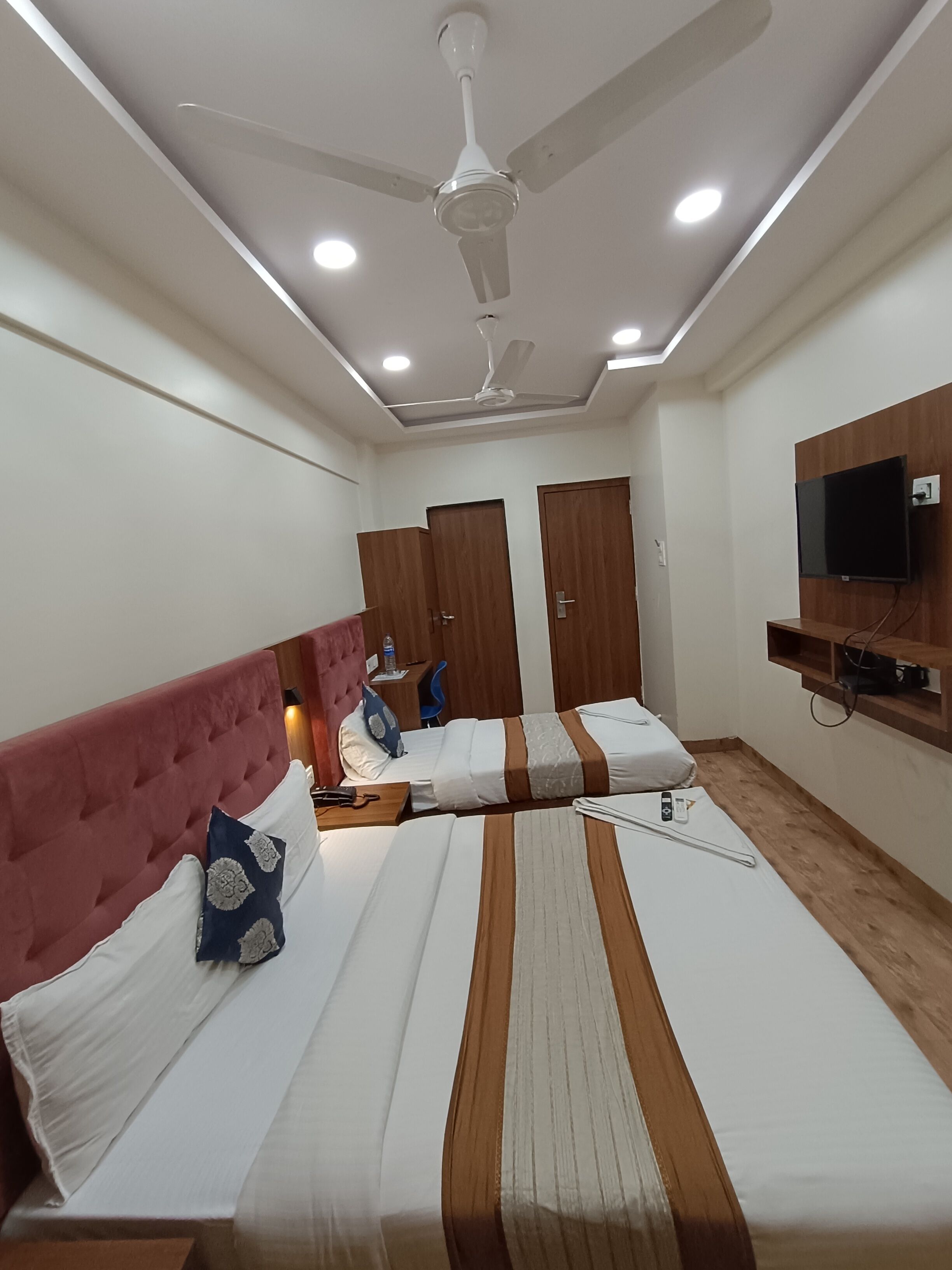 A hotel room with a bed, a desk, a chair, a ceiling fan, and a TV mounted on the wall.