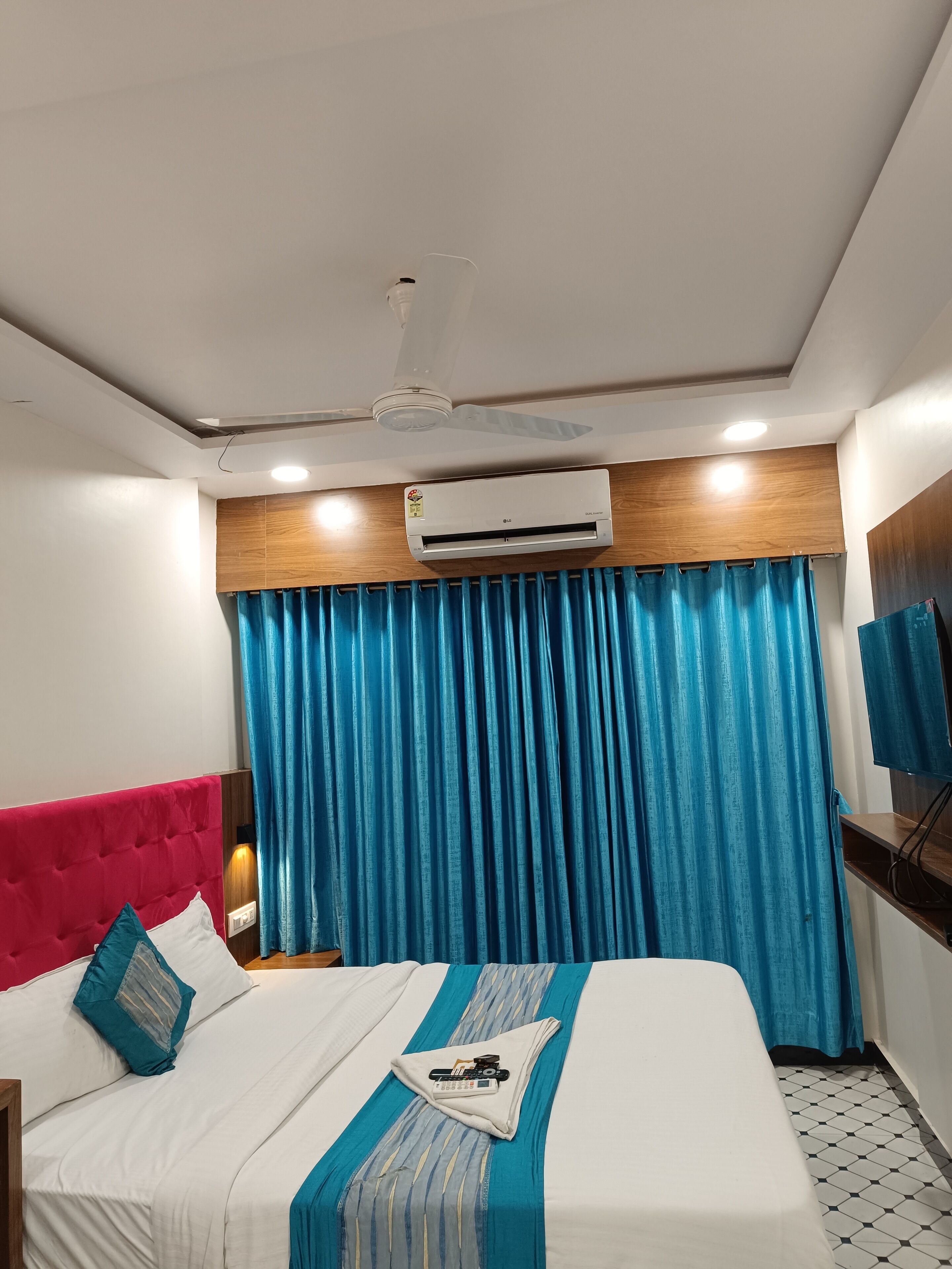 Una habitación de hotel con una cama, ventilador de techo, aire acondicionado y un televisor en la pared.