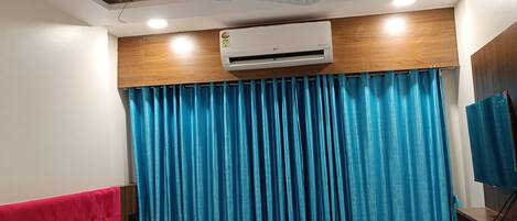 Una habitación de hotel con una cama, ventilador de techo, aire acondicionado y un televisor en la pared.