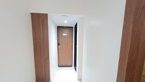 A hallway with a wooden door labeled '303', white walls, and a tiled floor. - Hotel Best (Mumbai)