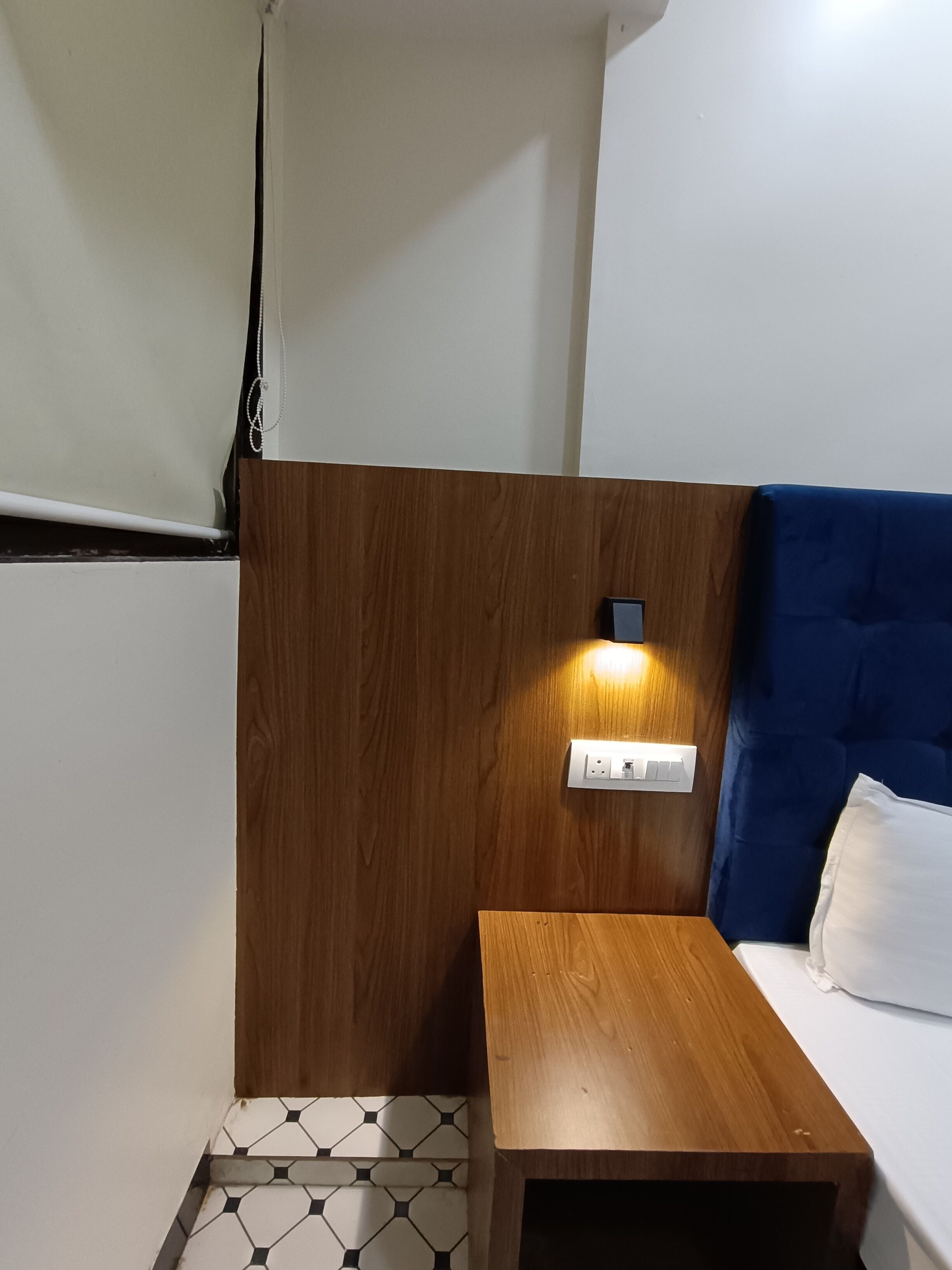 A small, neatly arranged room with a wooden headboard, a bedside table, and a bed with a blue headboard.
