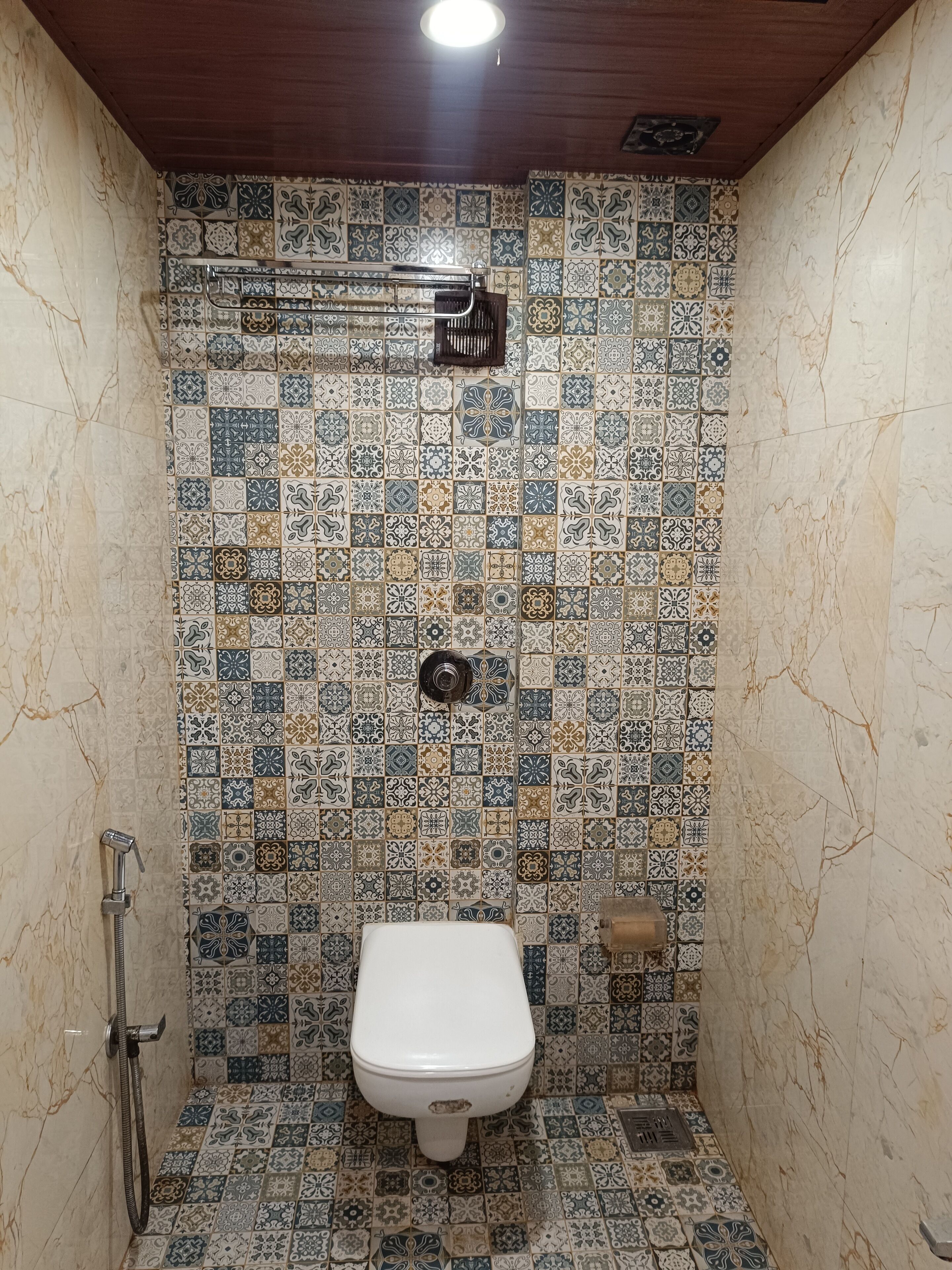 Un pequeño box de ducha con azulejos, un inodoro y un cabezal de ducha de mano.