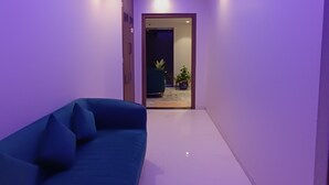 A hallway with a blue sofa, a ceiling light, and a door leading to a room with a plant. - Hotel Best (Mumbai)