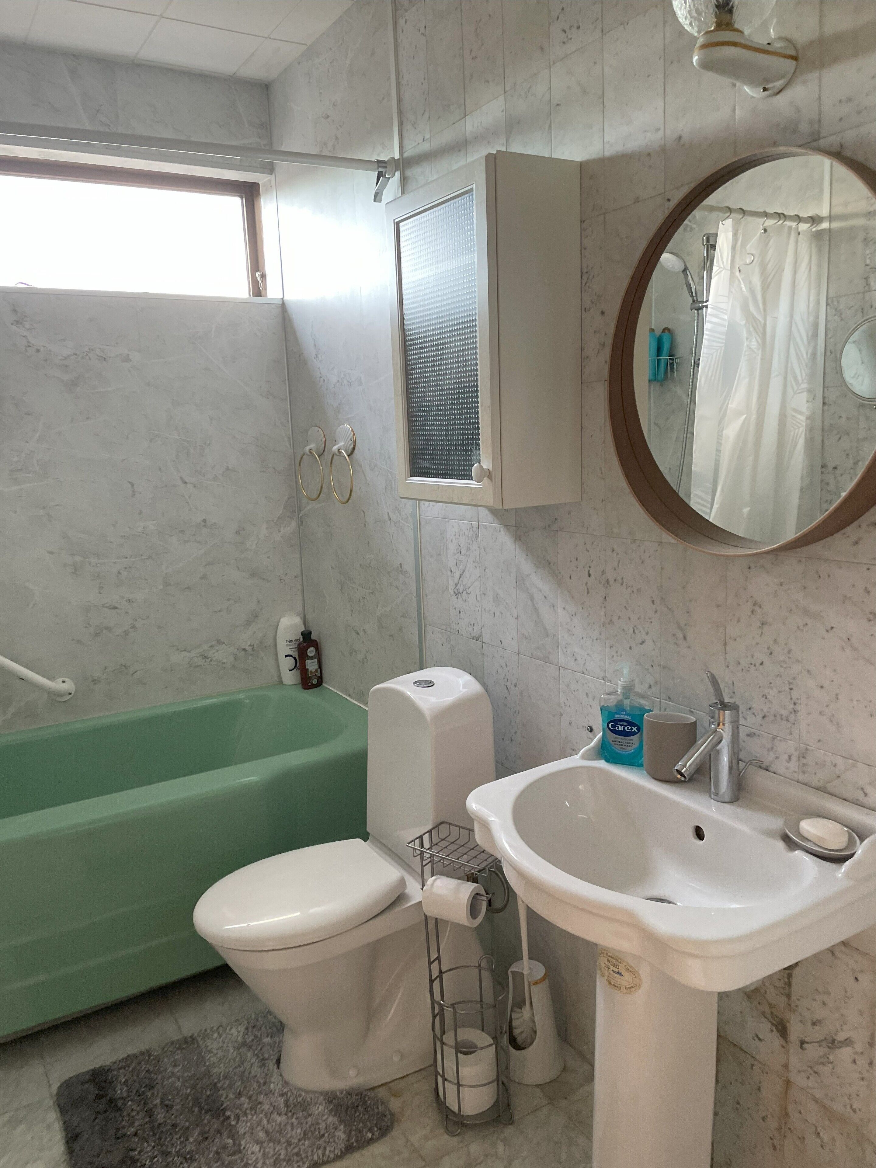 Een badkamer met een groen bad, een witte wastafel, een toilet, een spiegel en een raam met een handdoekhouder.