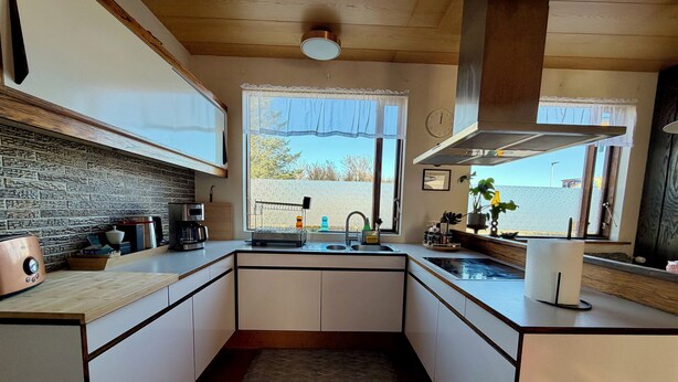 A modern kitchen with a stone backsplash, a coffee maker, a toaster, and a window with a view. - Keflavík 3BR Home, Near Airport, Sleeps 7 (Keflavík)