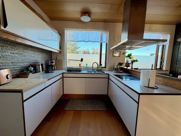 A modern kitchen with a stone backsplash, a coffee maker, a toaster, and a window with a view. - Keflavík 3BR Home, Near Airport, Sleeps 7 (Keflavík)