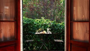 Een houten deur met ruitpanelen die uitkomt op een patio met een tafel gedekt voor twee personen, omgeven door weelderige begroeiing.