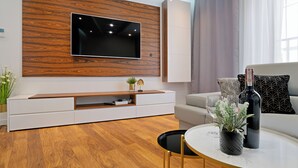 Un salon moderne avec un téléviseur fixé au mur en bois, un canapé blanc, une table basse avec une plante et une bouteille de vin.