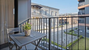 Un balcon avec une table et une chaise, un pot de fleurs et une vue sur une rue bordée d’immeubles.
