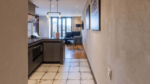 A modern kitchen with a central island, a dining area with a sofa and table, and a large window providing a city view.