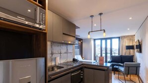 A modern kitchen with a built-in oven, a dishwasher, and a large island. There is a dining area with a sofa and a table, and a large window providing natural light.