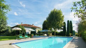A swimming pool with lounge chairs and umbrellas, surrounded by greenery and a house. - Holiday home in Cortona (Cortona)
