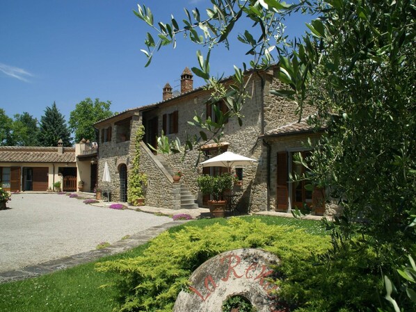 A stone building with a courtyard, outdoor seating, and a large umbrella. - Holiday home in Cortona (Cortona)