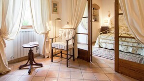 A cozy bedroom with a wooden bed frame, a plush chair, a small table, and a window with curtains. - Holiday home in Cortona (Cortona)