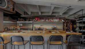 A bar area with a stainless steel counter, bar stools, and a variety of bottles and glasses.