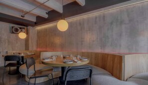 A restaurant interior with round tables, chairs, and pendant lighting.