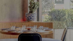 Comedor con mesa lista para cuatro personas, una planta en maceta y un colgador de luz.