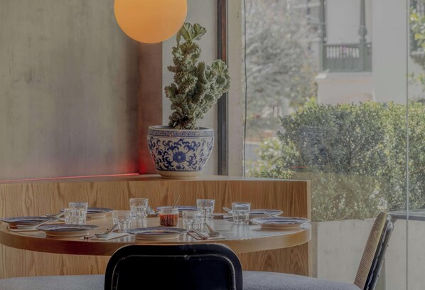 Un coin repas avec une table ronde dressée pour quatre personnes, une plante en pot et une grande fenêtre donnant sur un paysage verdoyant.
