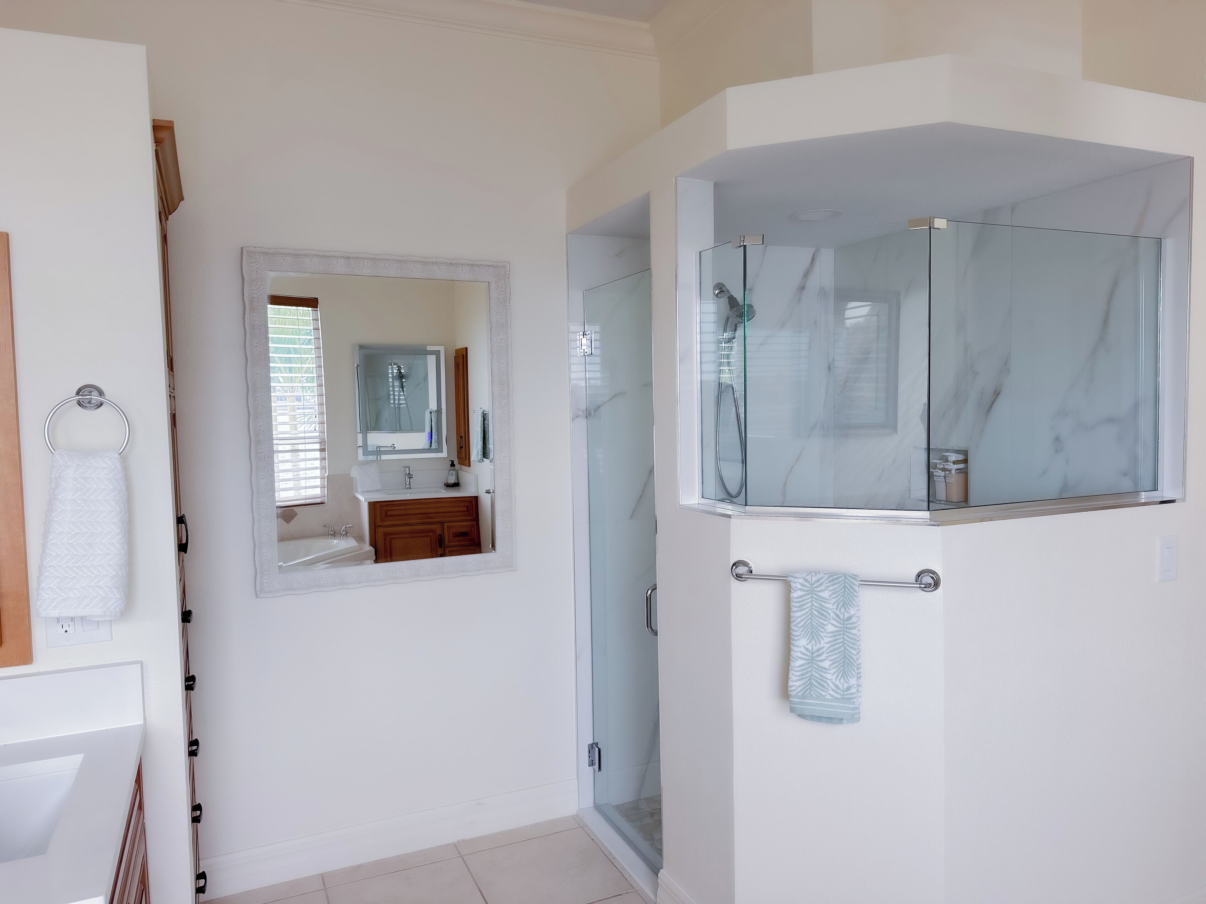Une salle de bain moderne avec une douche à l’italienne en verre, un meuble-lavabo blanc doté d’un plan de travail en marbre et un grand miroir au-dessus du lavabo.