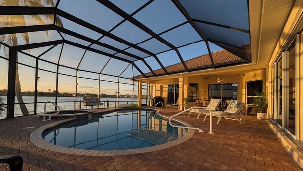 A covered outdoor swimming pool with lounge chairs and a view of the water. - CasaSuLago Sunset Lakefront, Saltwater Pool & Spa, Fishing, Kayaks & Game Room! (Cape Coral)