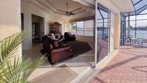 A spacious living area with a large window overlooking a body of water, a ceiling fan, and a built-in cabinet. - CasaSuLago Sunset Lakefront, Saltwater Pool & Spa, Fishing, Kayaks & Game Room! (Cape Coral)